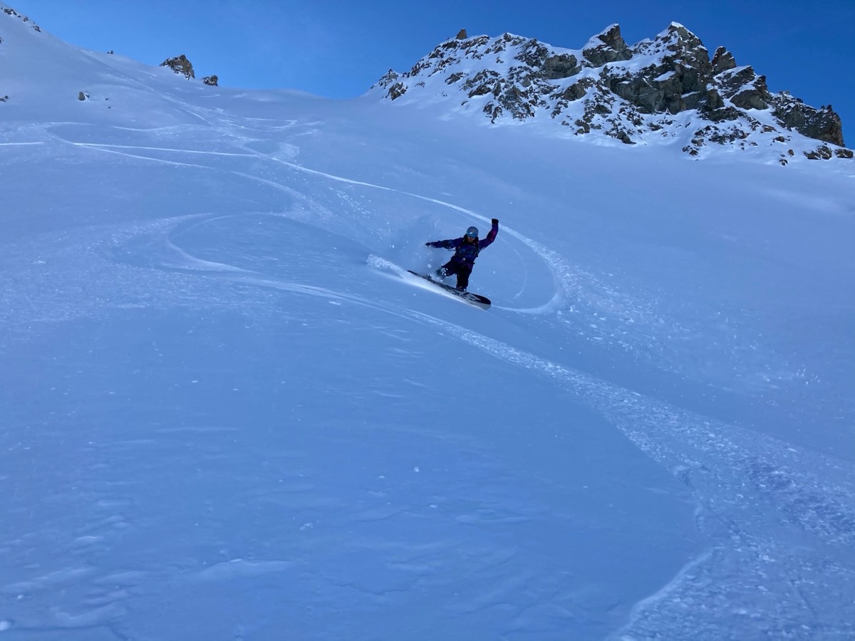Splitboard turn in deep snow below a rocky ridge